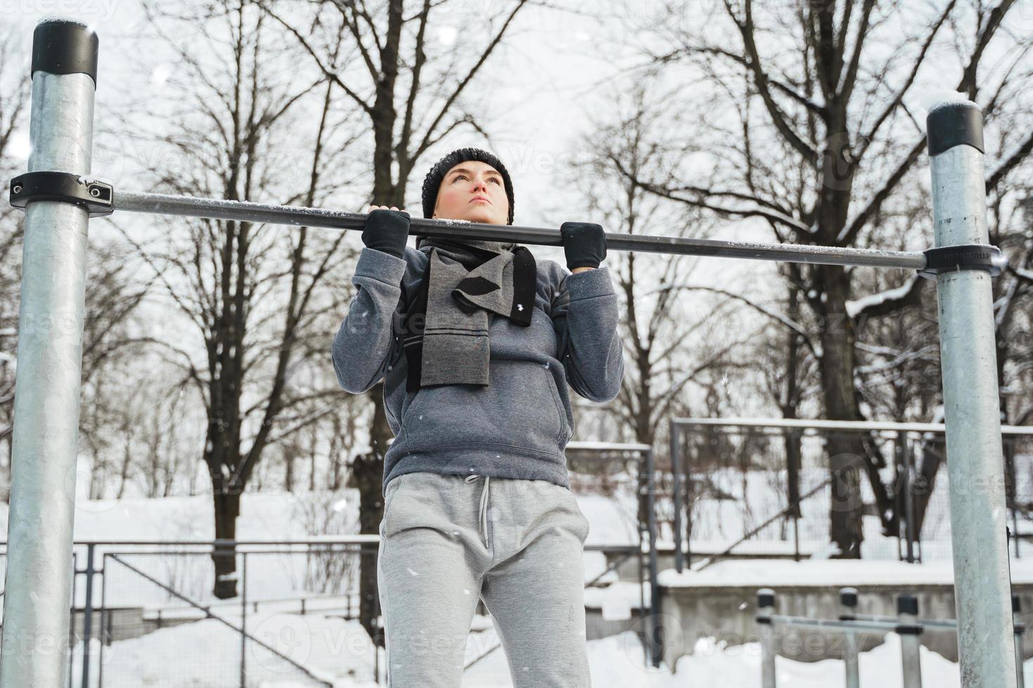 atletisk kvinna håller på med pull-ups på horisontell bar under utomhus- vinter- träna foto