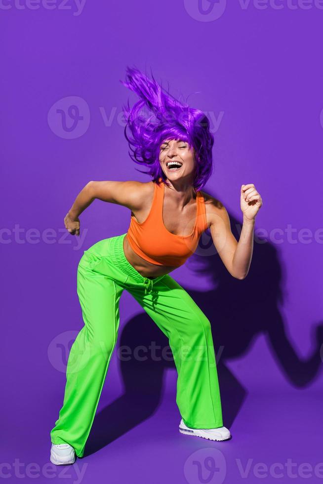 sorglös kvinna dansare bär färgrik sportkläder har roligt mot lila bakgrund foto