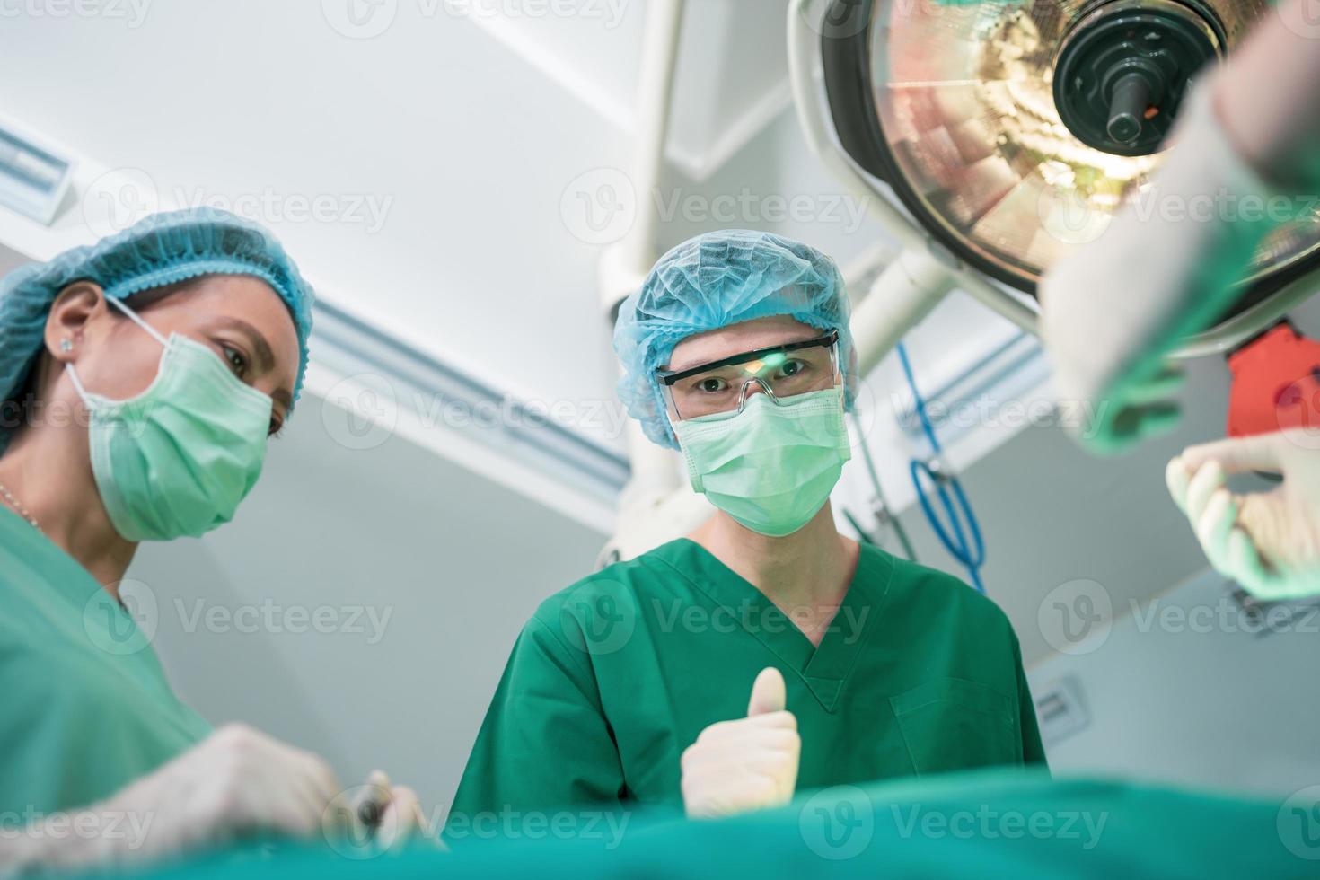 bild i låg vinkel av professionellt kirurgteam som utför operation i operationssalen, kirurg, assistenter och sjuksköterskor som utför operation på en patient, vårdkoncept för cancer och sjukdomsbehandling foto