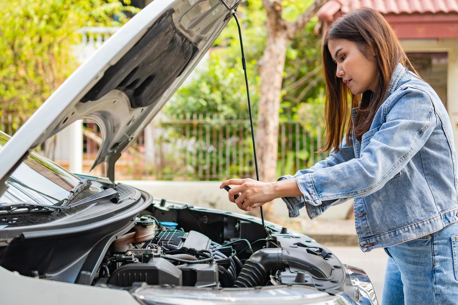 asiatisk kvinna och använder sig av smartphones till skicka motor bilder och skicka till bistånd efter en bil bryta ner på gata. begrepp av fordon motor problem eller olycka, nödsituation hjälp från professionell foto