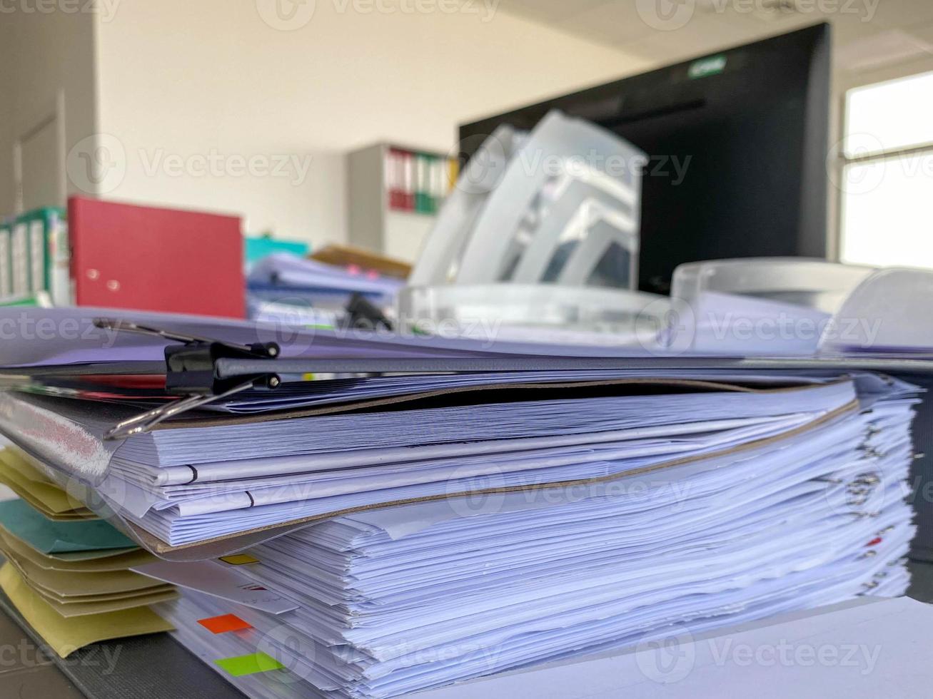stack av papper dokument i arkiv filer med klämma papper på tabell på kontor, upptagen kontor och lugg av data oavslutat mappar på kontor skrivbord inomhus- nära fönster, företag begrepp foto