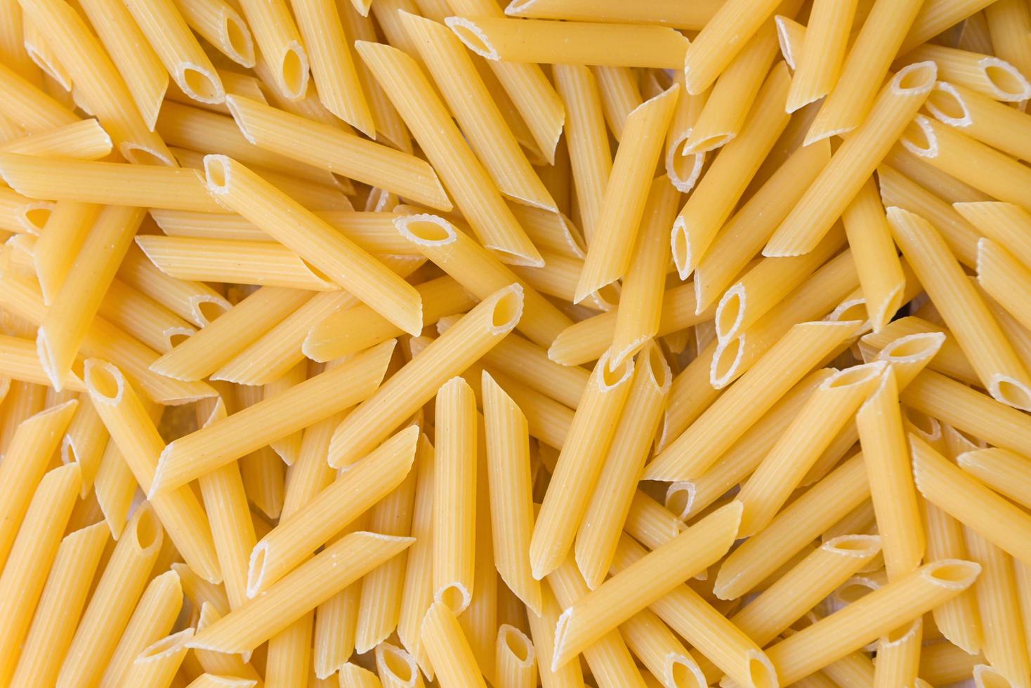 penne pasta bakgrund - topp se, rå penne pasta textur bakgrund, stänga upp rå penne rigat pasta okokt utsökt pasta för matlagning mat foto