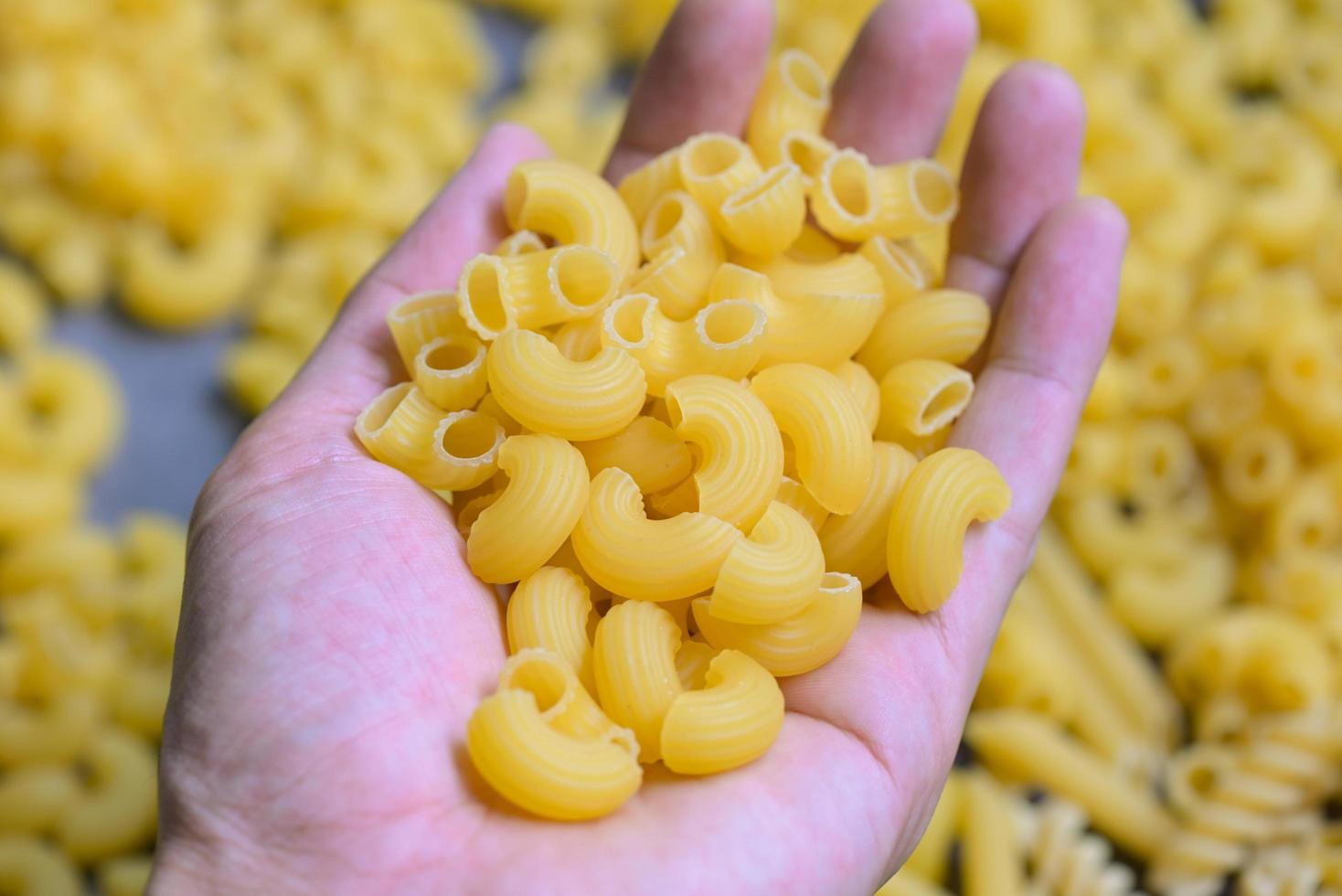 pasta på hand och rå makaroner bakgrund, stänga upp rå makaroner pasta okokt utsökt pasta för matlagning mat foto