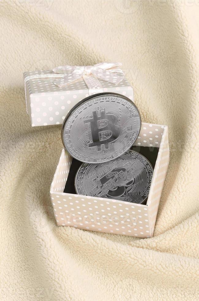 de silver- bitcoin lögner i en små orange gåva låda med en små rosett på en filt tillverkad av mjuk och fluffig ljus orange skinna tyg med en stor siffra av lättnad veck foto