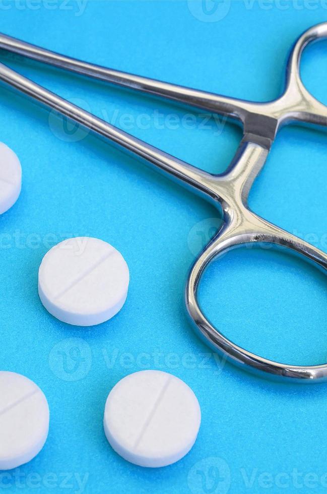 flera vit tabletter och en medicinsk klämma lögn på en ljus blå bakgrund yta. bakgrund bild på medicinsk och farmaceutisk ämnen foto