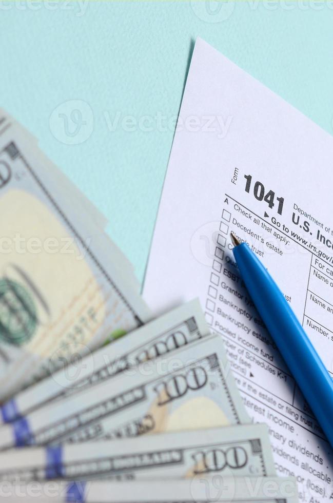 1041 beskatta form lögner nära hundra dollar räkningar och blå penna på en ljus blå bakgrund. oss inkomst beskatta lämna tillbaka för fastigheter och litar på foto