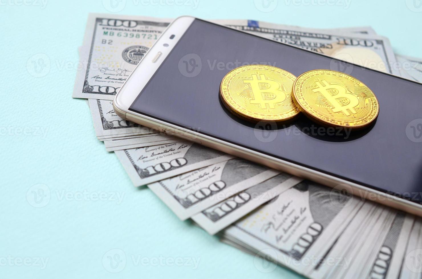 bitcoins lögner på en smartphone och hundra dollar räkningar på en ljus blå bakgrund foto