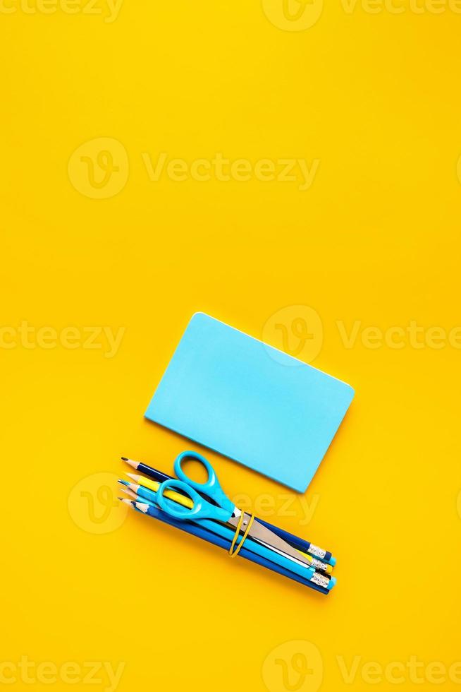 gul bakgrund med sax och pennor, anteckningsblock för skolreklam. foto