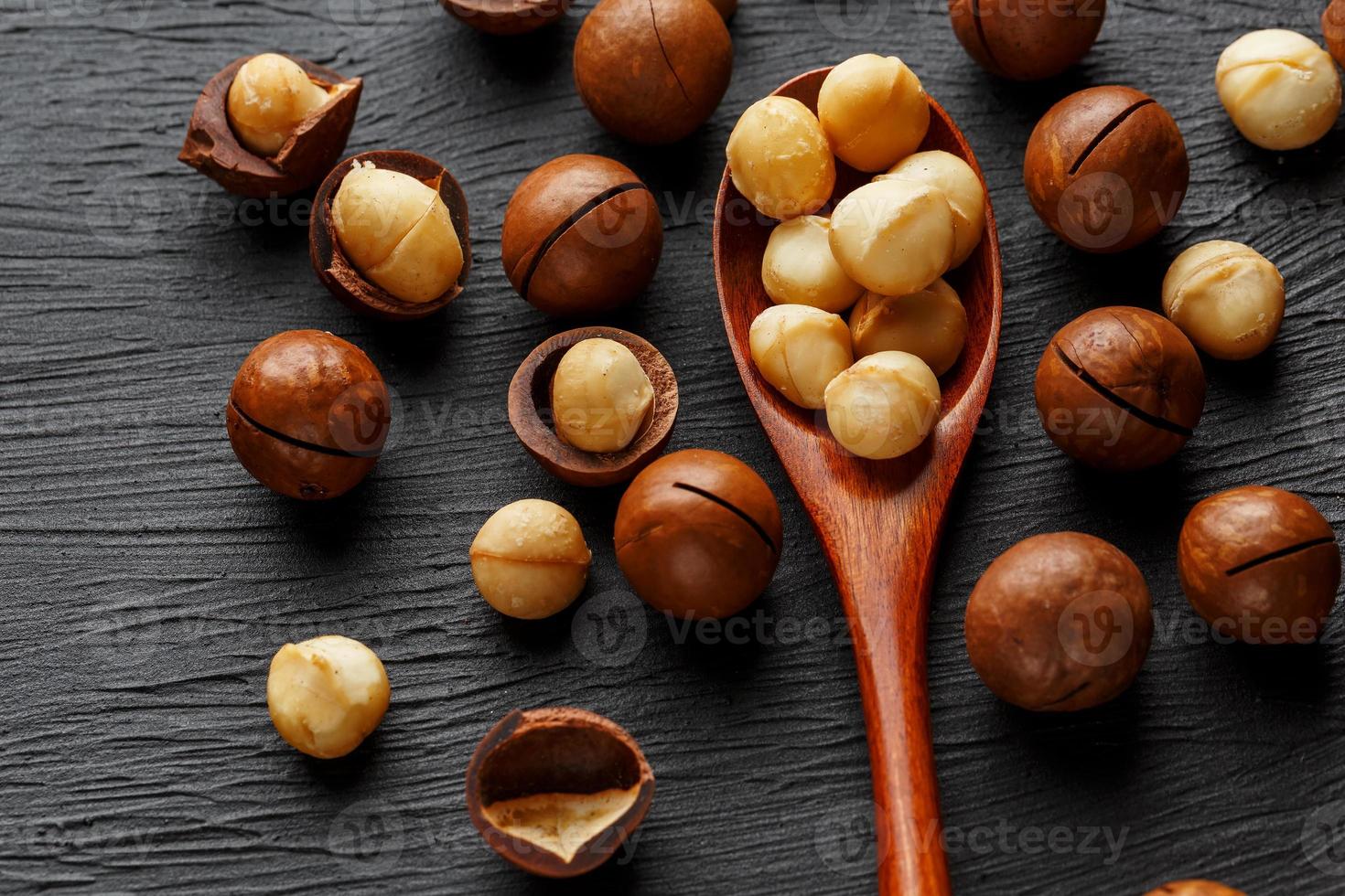 skalade macadamia nöt och skalad macadamia nöt på en svart textural bakgrund i en trä- sked foto