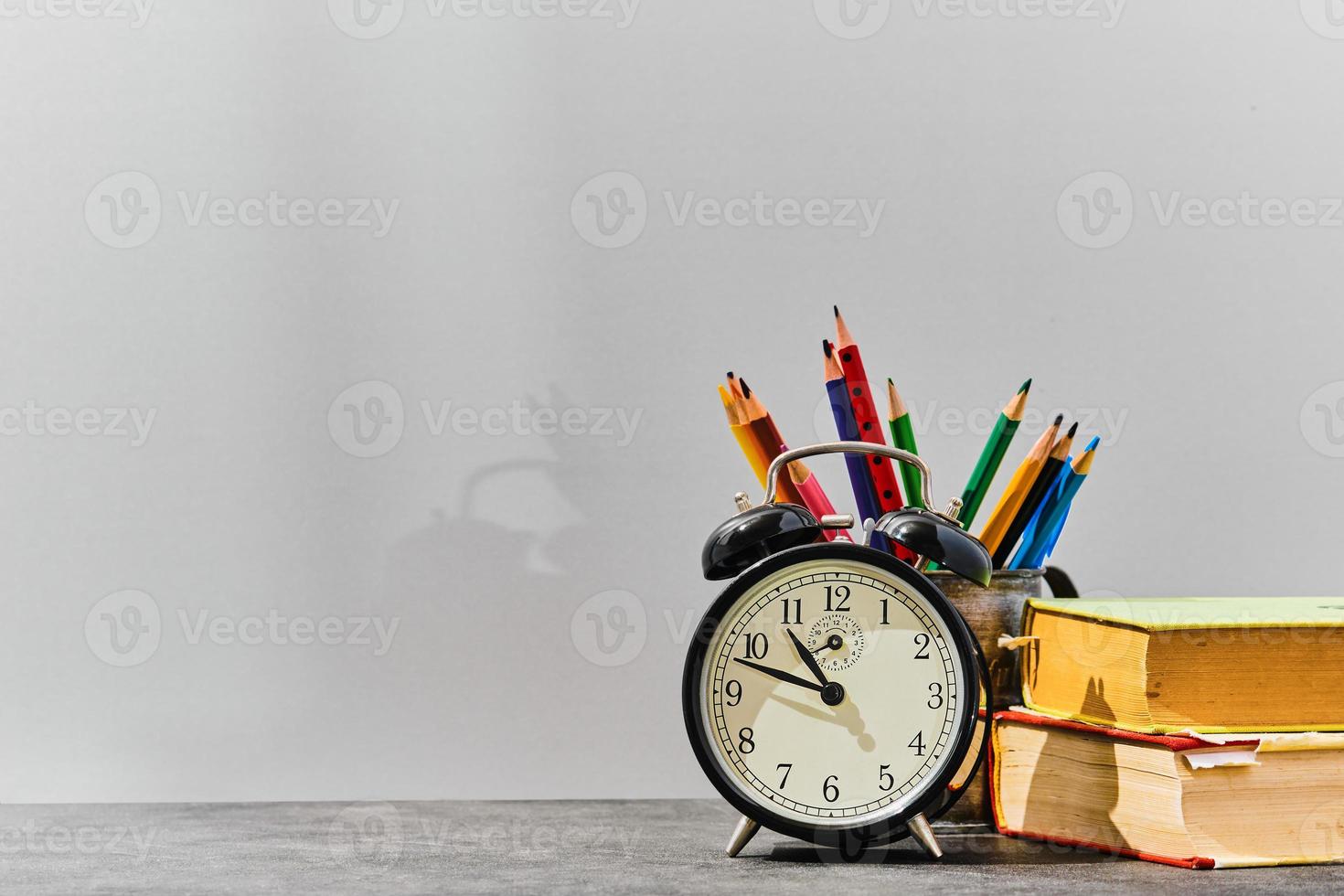 begrepp tillbaka till skola eller lärarens dag aning. pennor, pennor, böcker, ett larm klocka på de tabell, mot de bakgrund av en grå styrelse med kopia Plats. foto