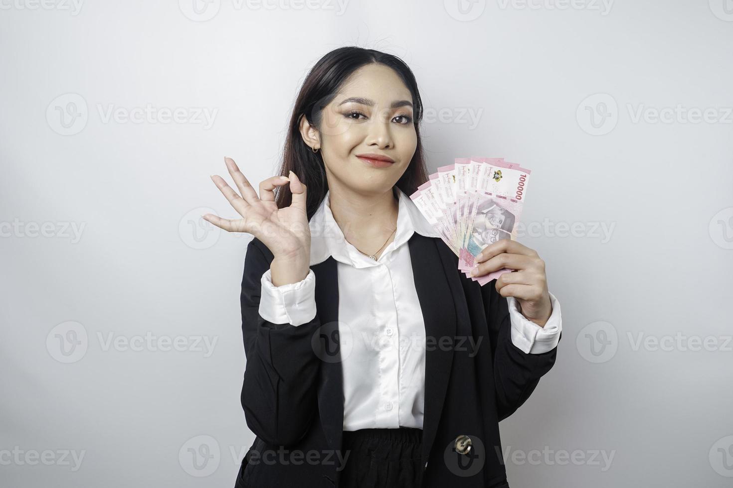 upphetsad asiatisk affärskvinna bär en svart kostym ger ett ok hand gest isolerat förbi en vit bakgrund foto