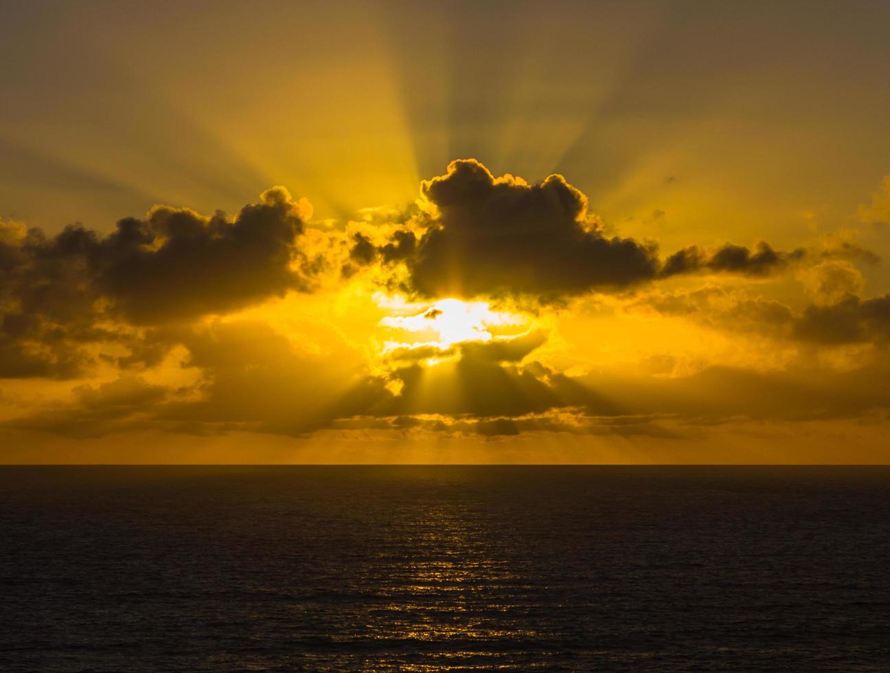 solnedgång genom moln över havet foto