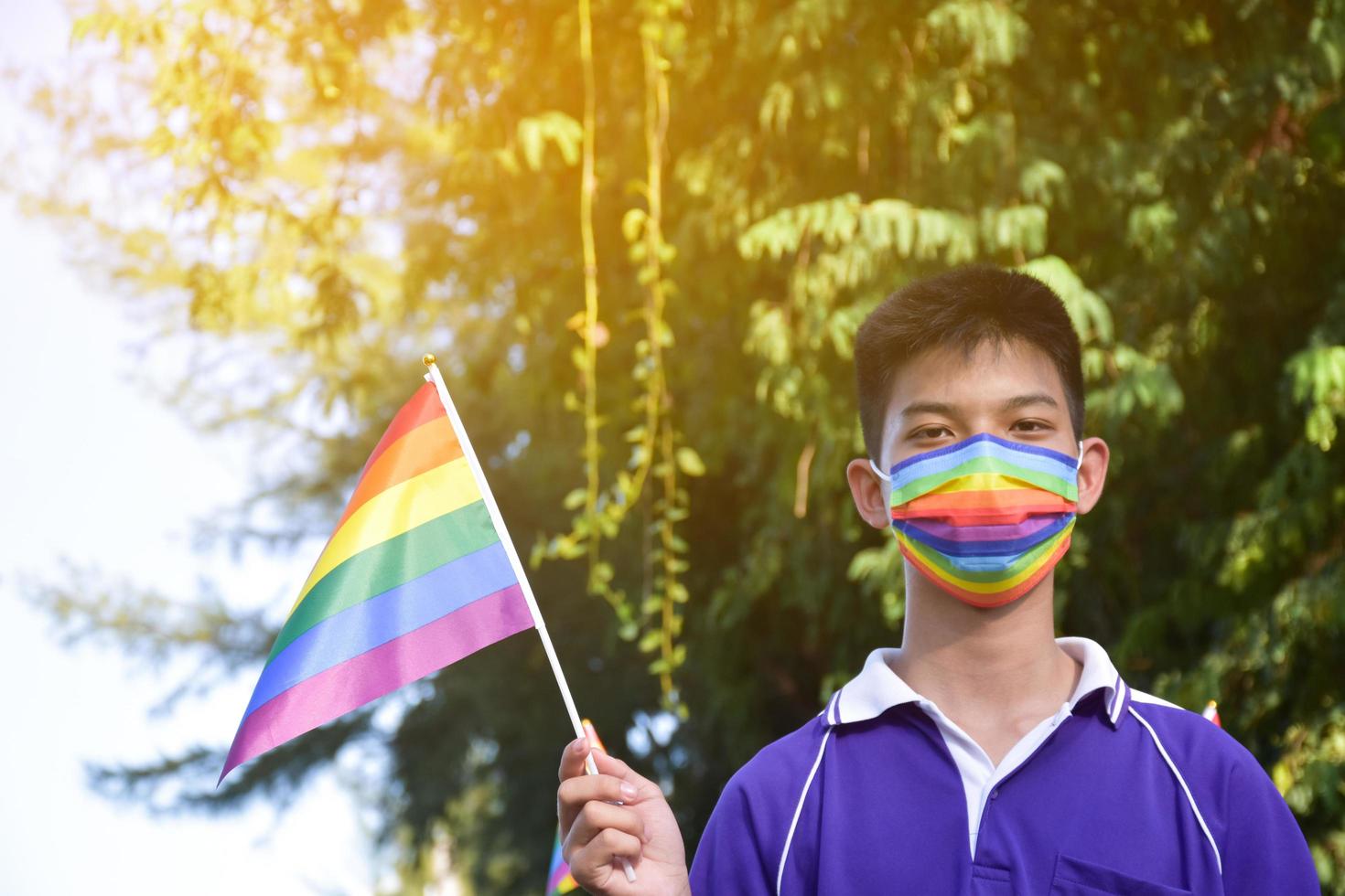 porträtt asiatisk ung pojke innehar regnbåge flagga, HBTQ symbol, i händer medan sammanfogning hans HBTQ aktivitet på skola, begrepp för HBTQ gemenskap firande i stolthet månad, juni, 2023, runt om de värld. foto