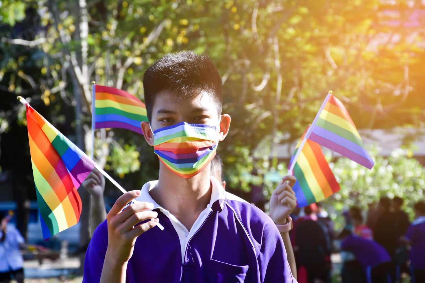 porträtt asiatisk ung pojke innehar regnbåge flagga, HBTQ symbol, i händer medan sammanfogning hans HBTQ aktivitet på skola, begrepp för HBTQ gemenskap firande i stolthet månad, juni, 2023, runt om de värld. foto