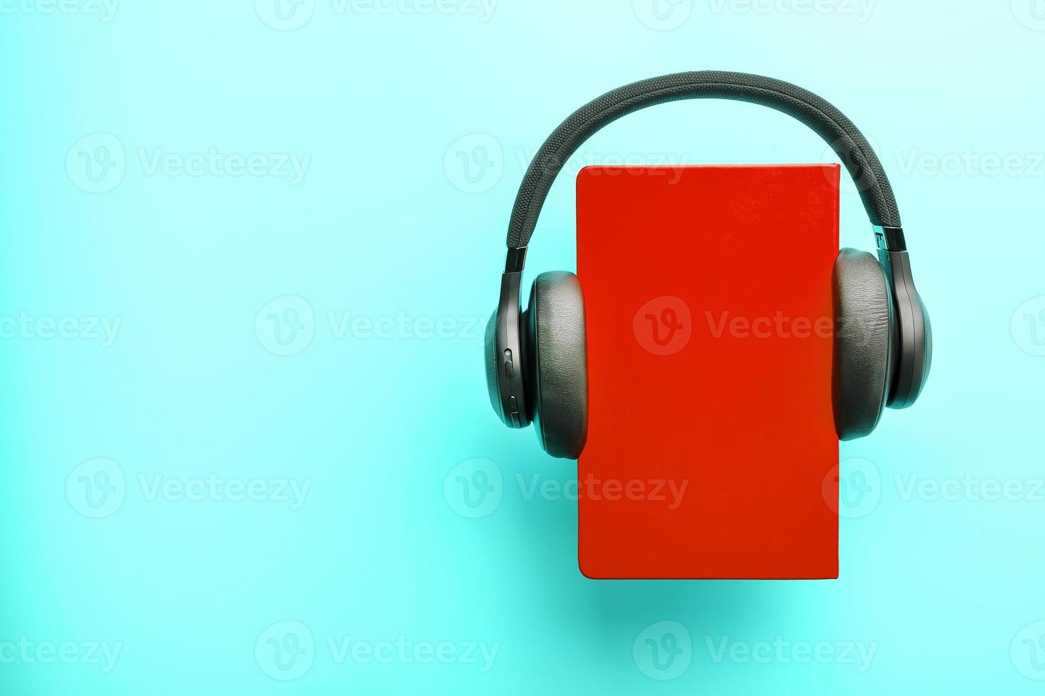 hörlurar är bärs på en bok i en röd hårt omslag på en blå bakgrund, topp se. foto