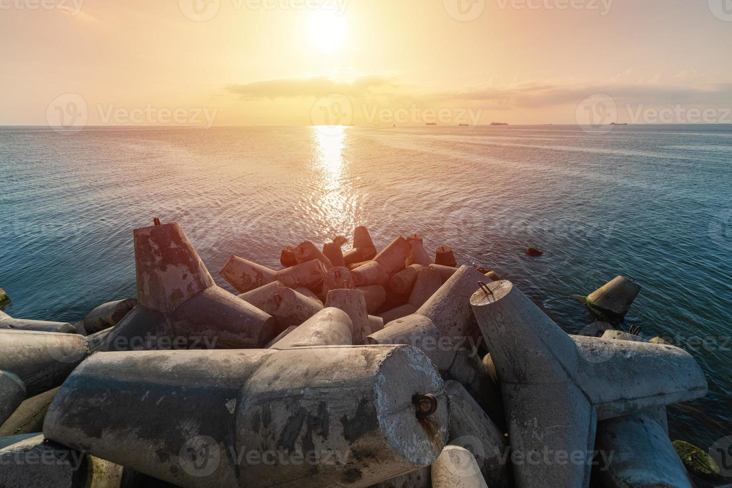 vacker solnedgång havslandskap. vågbrytare tetrapods i land vid piren. lastfartyg vid horisonten. resedrömmar och motivation foto