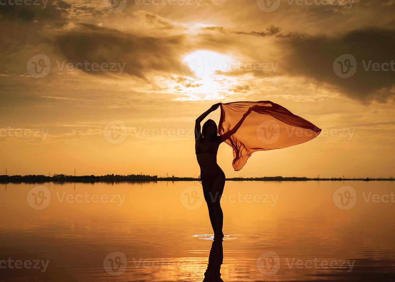 silhuett av en flicka i en röd baddräkt på de strand. röd vävnad utvecklas i henne händer. foto