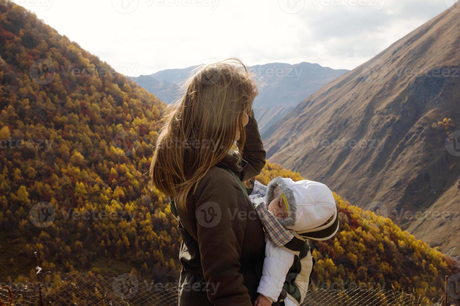 porträtt av ung skön kvinna med henne liten sovande dotter i alltså bärare på en bakgrund av höst berg. kaukasus berg, georgien. foto