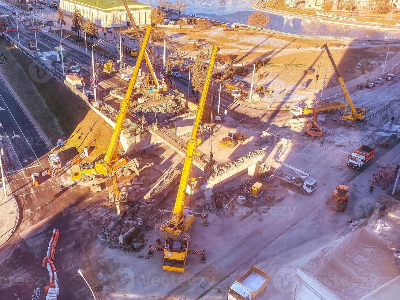 konstruktion av en ny planskild i de stad Centrum. nära de flod, gående väg och många byggnader. lång, gul konstruktion kranar är byggnad en bro från tung balkar foto