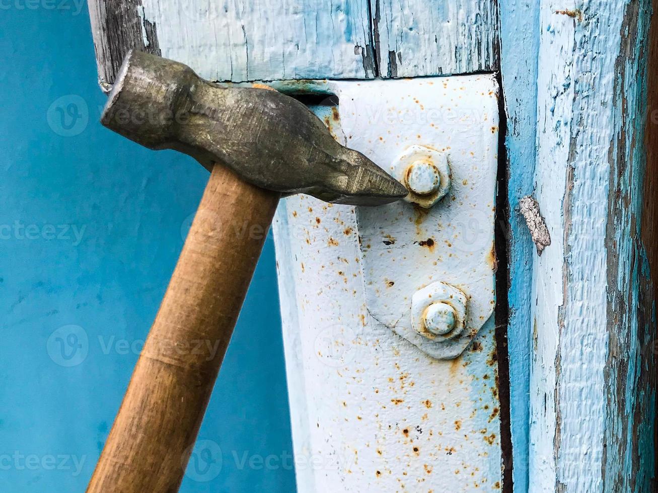 hammare på en trä- hantera med en metall slutet. hammare naglar in i en metall yta. metall ark är målad grå. på en blå trä bakgrund foto