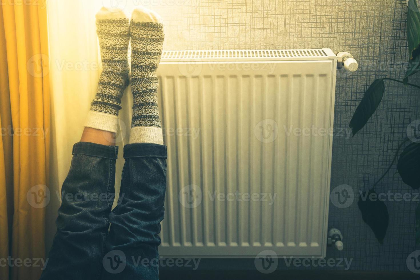 ben med färgrik stickat vinter- xmas strumpor på fötter uppvärmningen på central uppvärmning radiator värmare. vinter- tid, kall väder säsong fester ensamhet på Hem ensam foto