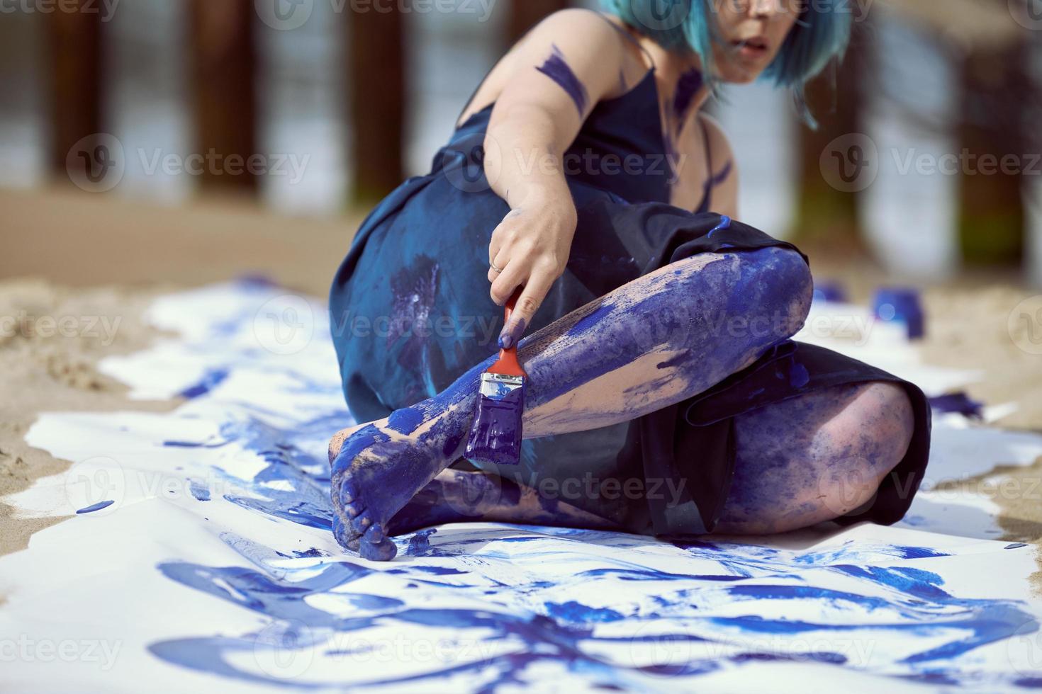 kvinnlig performancekonstnär i mörkblå klänning insmord med blå gouachemålning med breda streck på duk foto