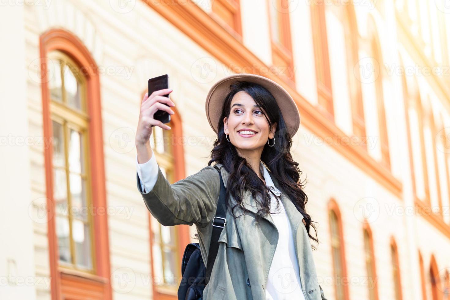 sorglös och Lycklig, solig vår humör. söt ung leende flicka är framställning selfie på en kamera medan gående utomhus. hon är bär tillfällig utrusta foto