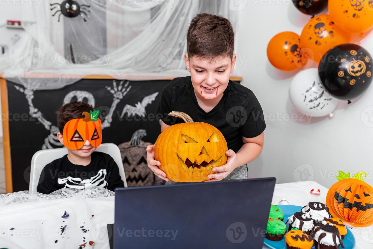 Lycklig ung Pojkar, bröder talande med farföräldrar eller vänner via video ring upp använder sig av bärbar dator på halloween dag , upphetsad unge som visar hans ny domkraft o' lykta halloween pumpa med ristade leende foto