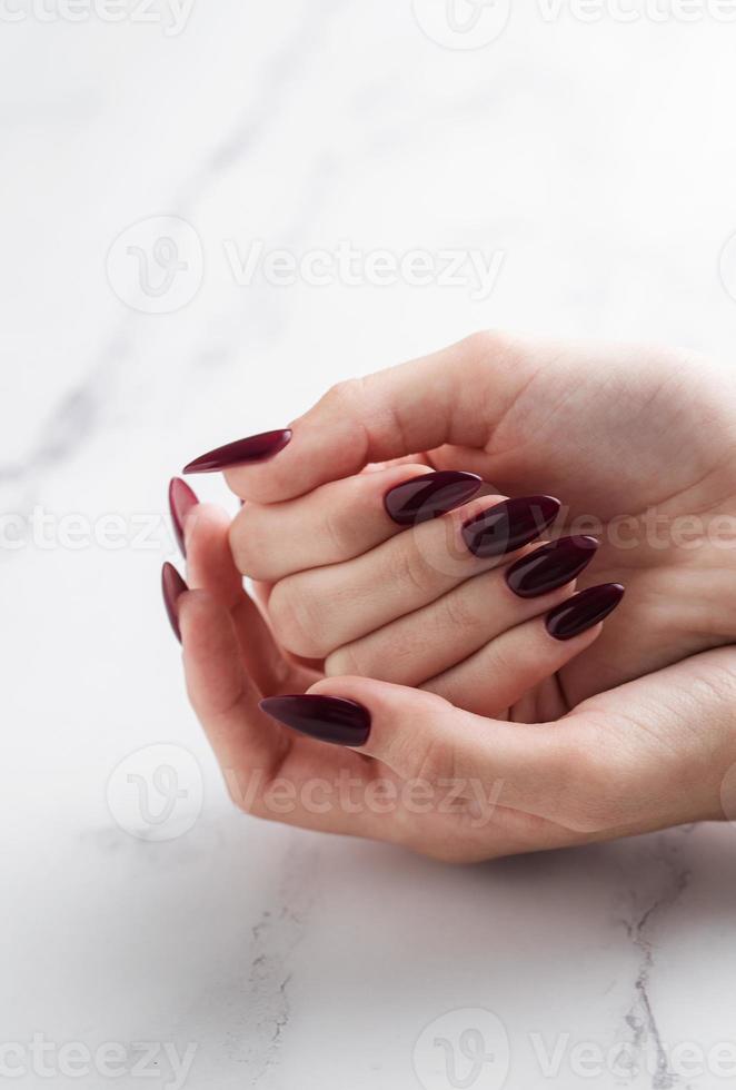 händer av en ung kvinna med mörk röd manikyr på naglar foto