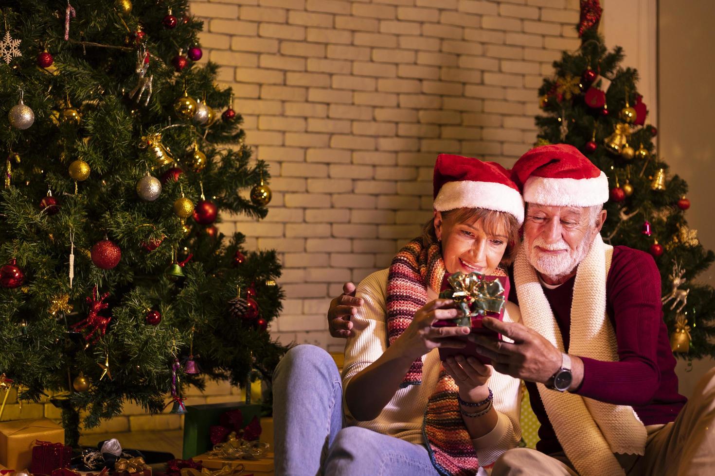 senior caucasian par fira jul tillsammans i lycka och spänning på Hem med röd santa hatt och jul träd foto