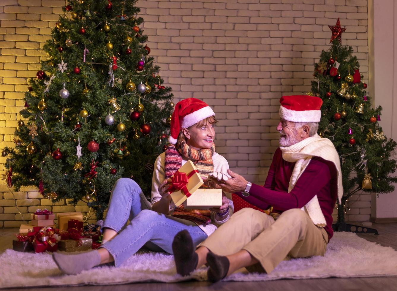 senior caucasian par fira jul tillsammans i lycka och spänning på Hem med röd santa hatt och jul träd foto