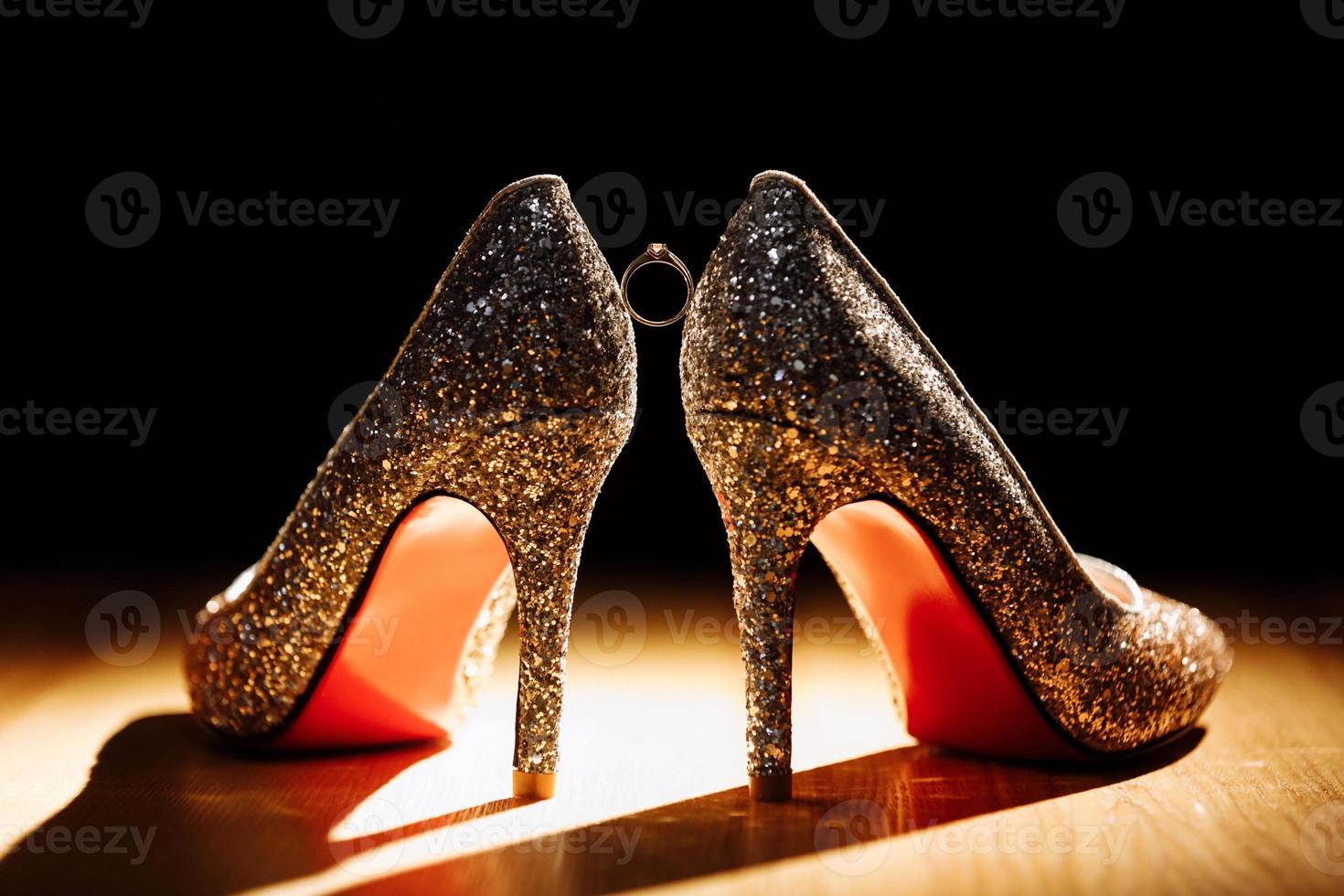 gyllene ringa med diamant mellan par av brud skor på mörk bakgrund. selektiv fokus foto