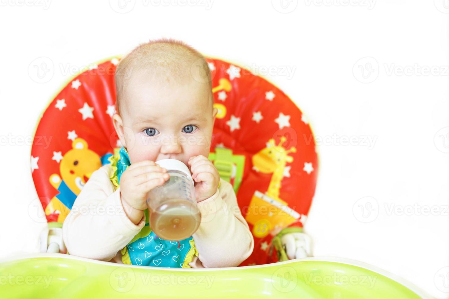 bebis dricka från flaska Sammanträde i hög stol på en vit bakgrund foto