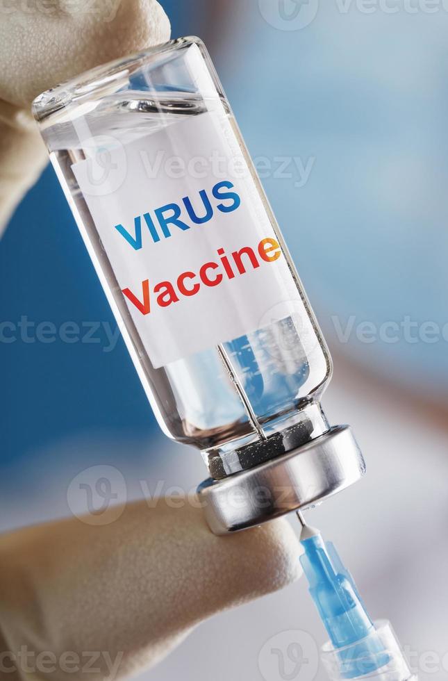 ett ampull med de inskrift virus vaccin och en spruta i de händer av en forskare läkare i sudd handskar med en vaccin närbild. foto