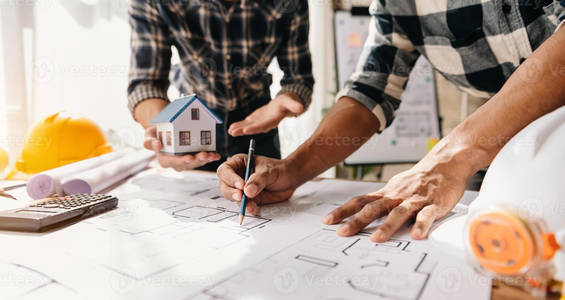 professionell arkitekt, ingenjör eller interiör granskning plan på arbetsplats skrivbord Bakom hus modell i kontor Centrum foto