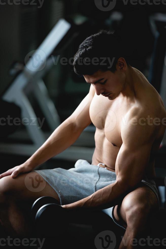 ung man träna, lyft med hantel till bygga muskel i kondition på Gym. foto