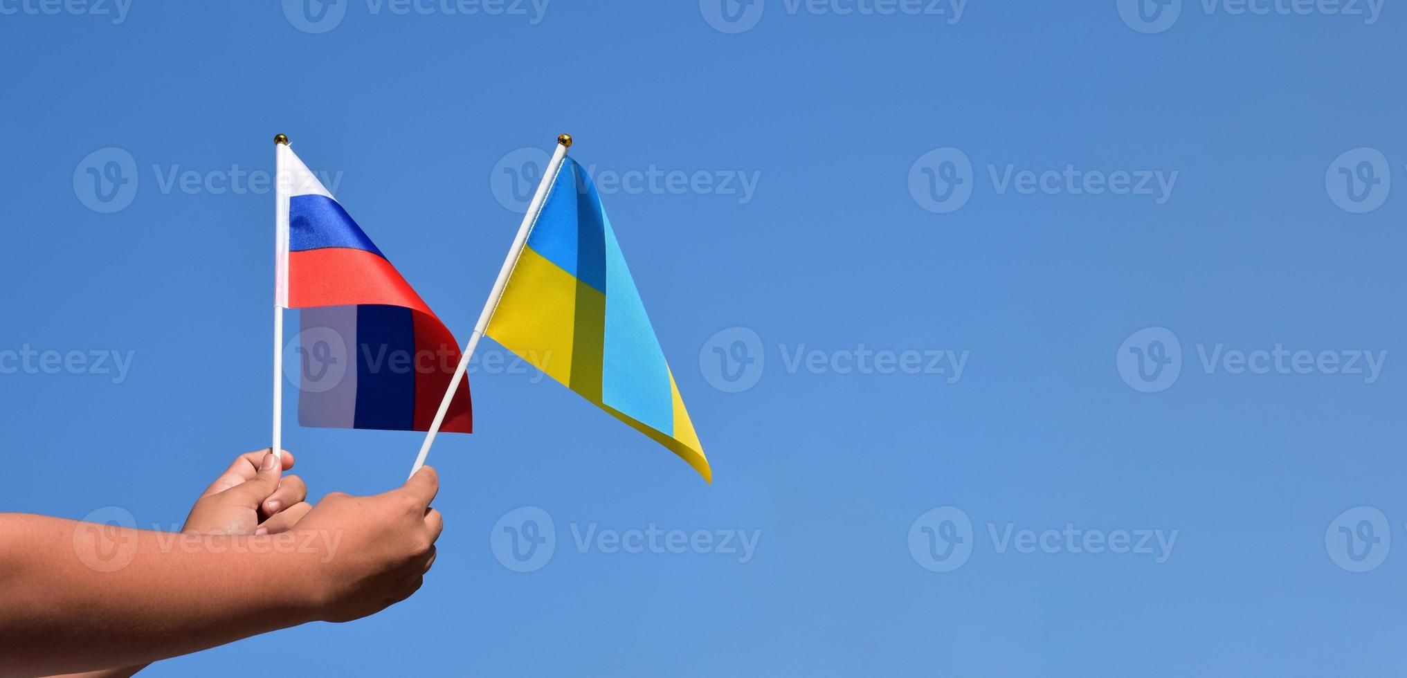 ryssland flagga och ukraina flagga, innehav i händer, blå himmel bakgrund, begrepp för stoppa de krig mellan ryssland och Ukraina, mjuk och selektiv fokus, kopia Plats. foto