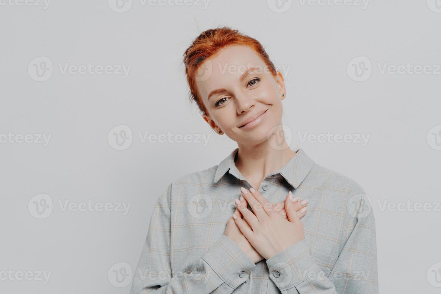 ung härlig rödhårig kvinna som håller korsade händer på bröstet och känner sig tacksam och tacksam foto