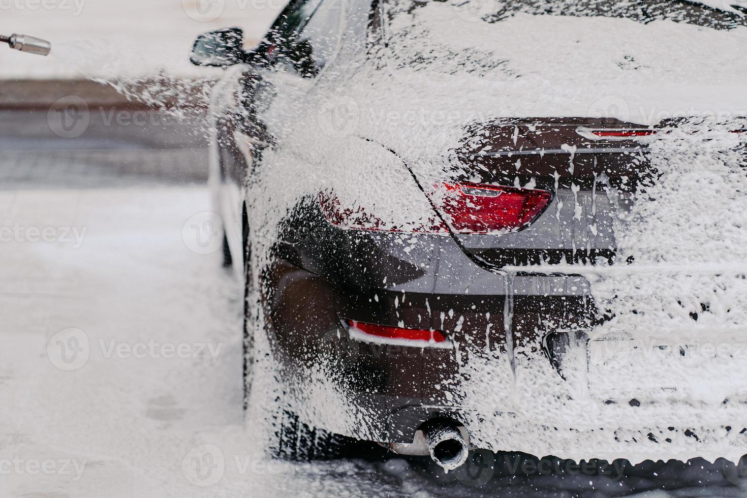 horisontell bild av bil täckt med tvålskum. städtjänst. vattentrycket på bilen. manuell biltvätt. högtryckstvätt foto