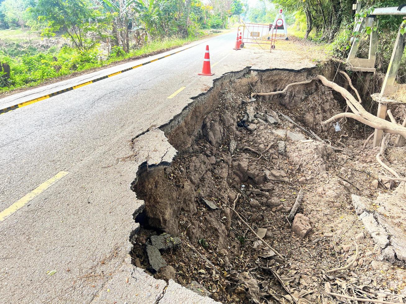 asfalt väg kollapsade och sprickor i de vid vägkanten, väg jordskred subside med väg kon orsakade förbi flod erosion foto