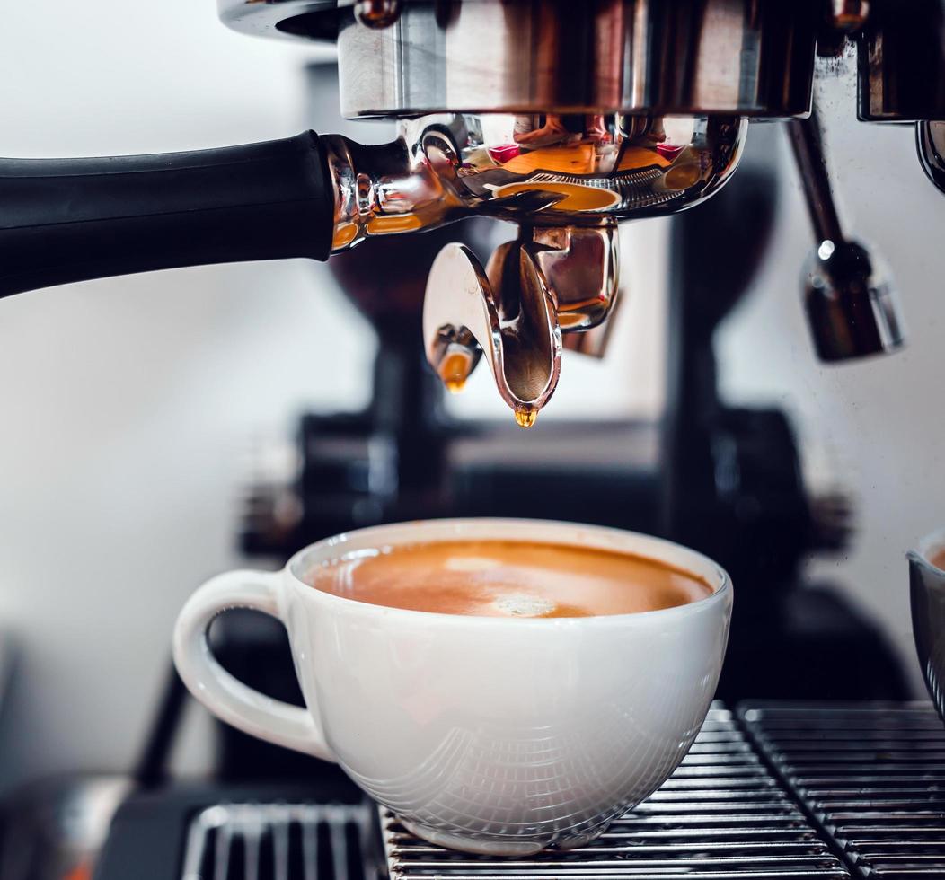 kaffe extraktion från de kaffe maskin med en portafilter häller kaffe in i en kopp, espresso porering från kaffe maskin på kaffe affär foto
