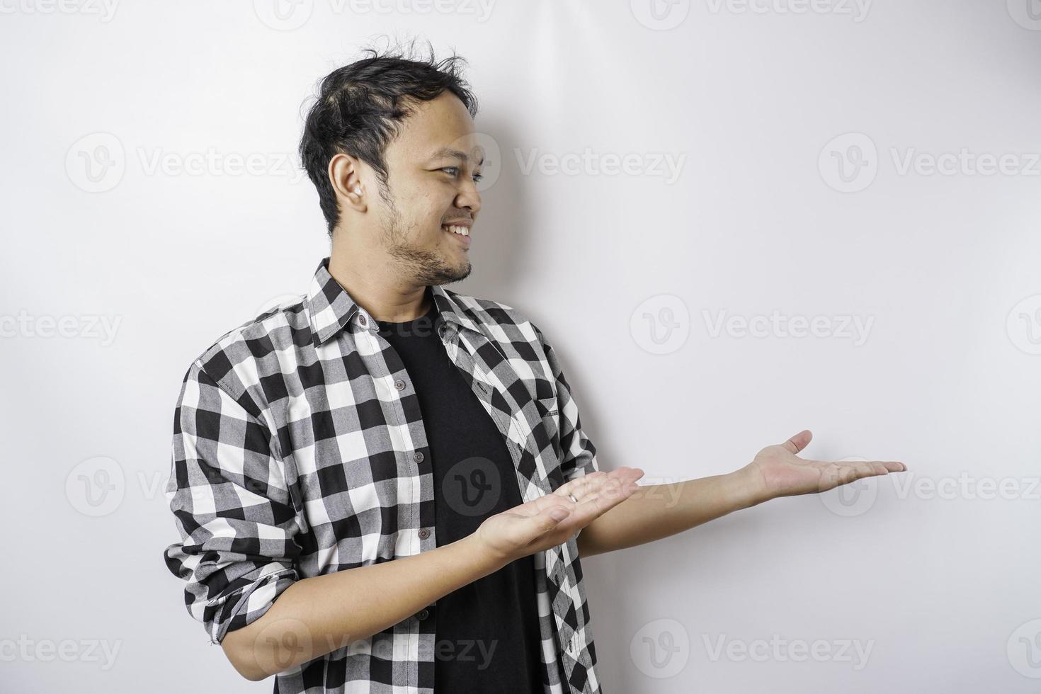 upphetsad asiatisk man bär tartan skjorta är pekande på de kopia Plats bredvid honom, isolerat förbi vit bakgrund foto