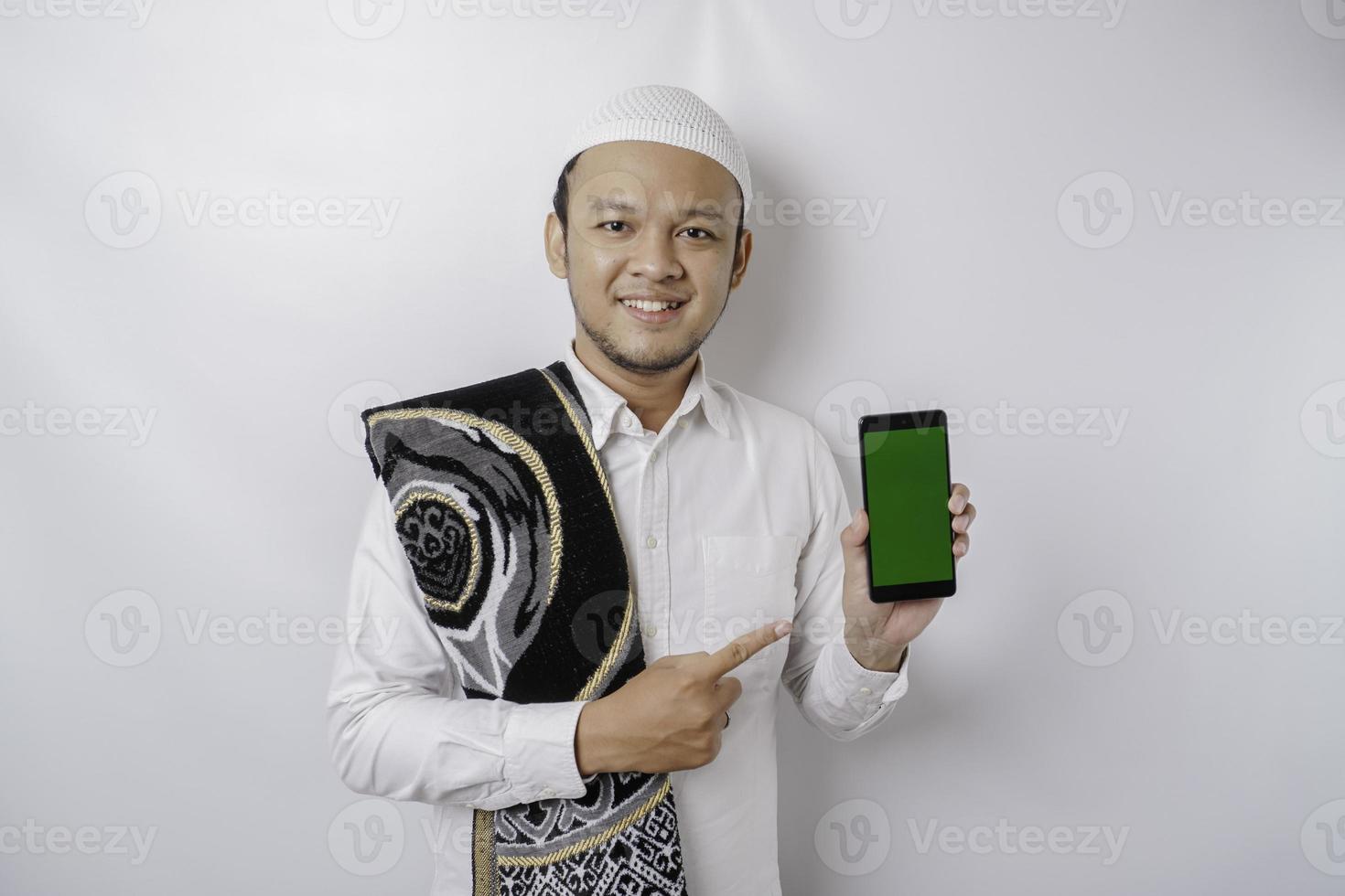 en porträtt av en Lycklig asiatisk muslim man leende medan som visar kopia Plats på hans telefon, isolerat förbi vit bakgrund foto