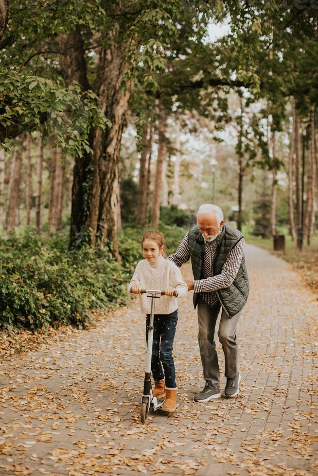 senior man undervisning hans barnbarn på vilket sätt till rida sparka skoter i parkera foto