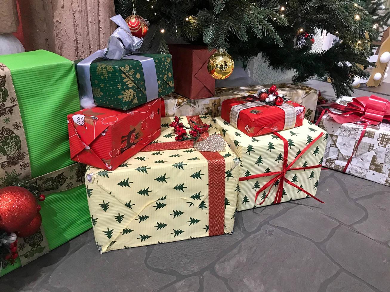 jul och ny år högtider, en stor siffra av gåvor i en flerfärgad omslag med bågar är under en stor jul träd med skön leksaker på de träd foto