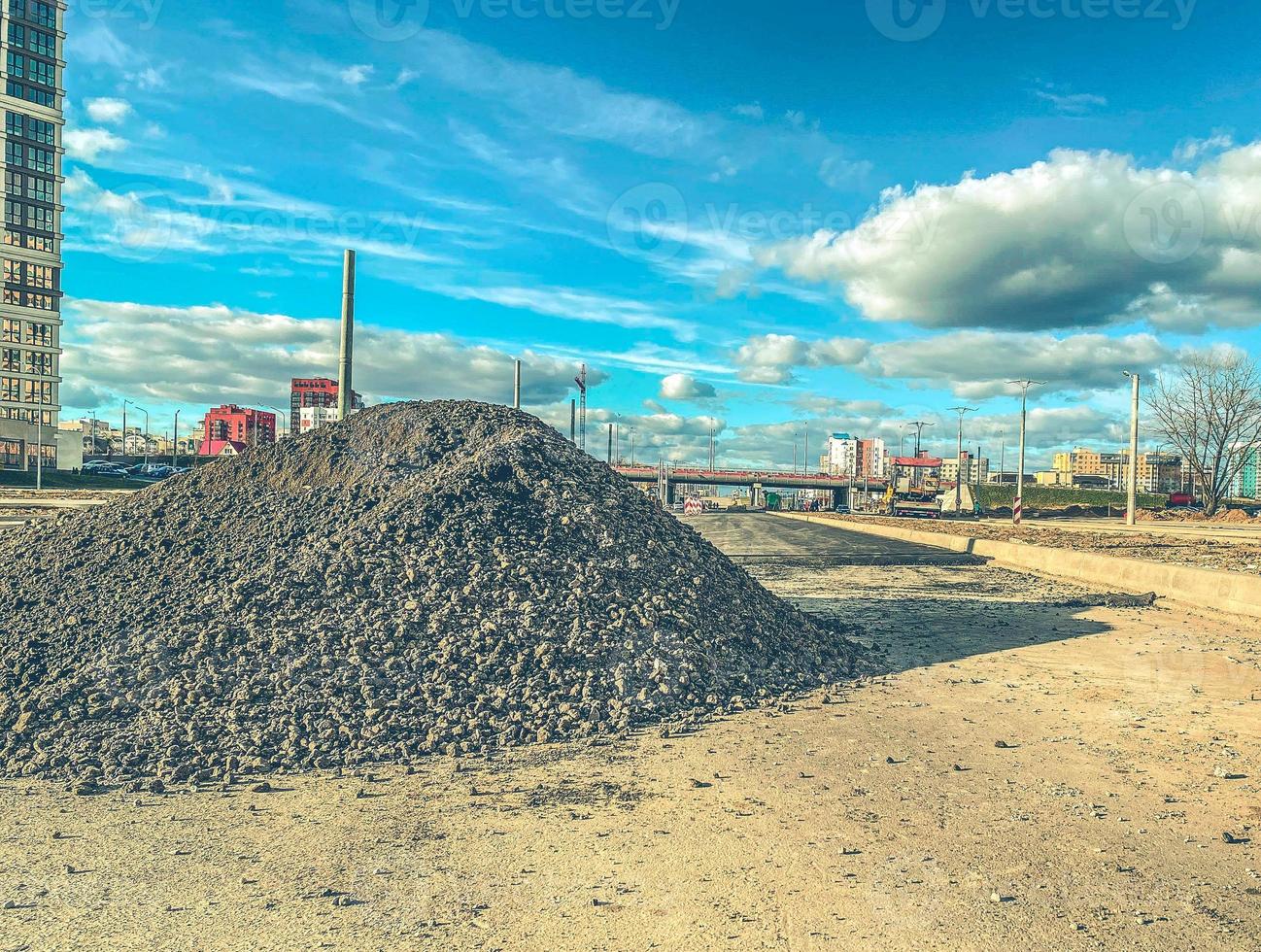 konstruktion webbplats. en mound av stenar och sand Nästa till lång hus under konstruktion. de bearbeta av byggnad ny flera våningar byggnader. stenar för konstruktion och asfalt om foto