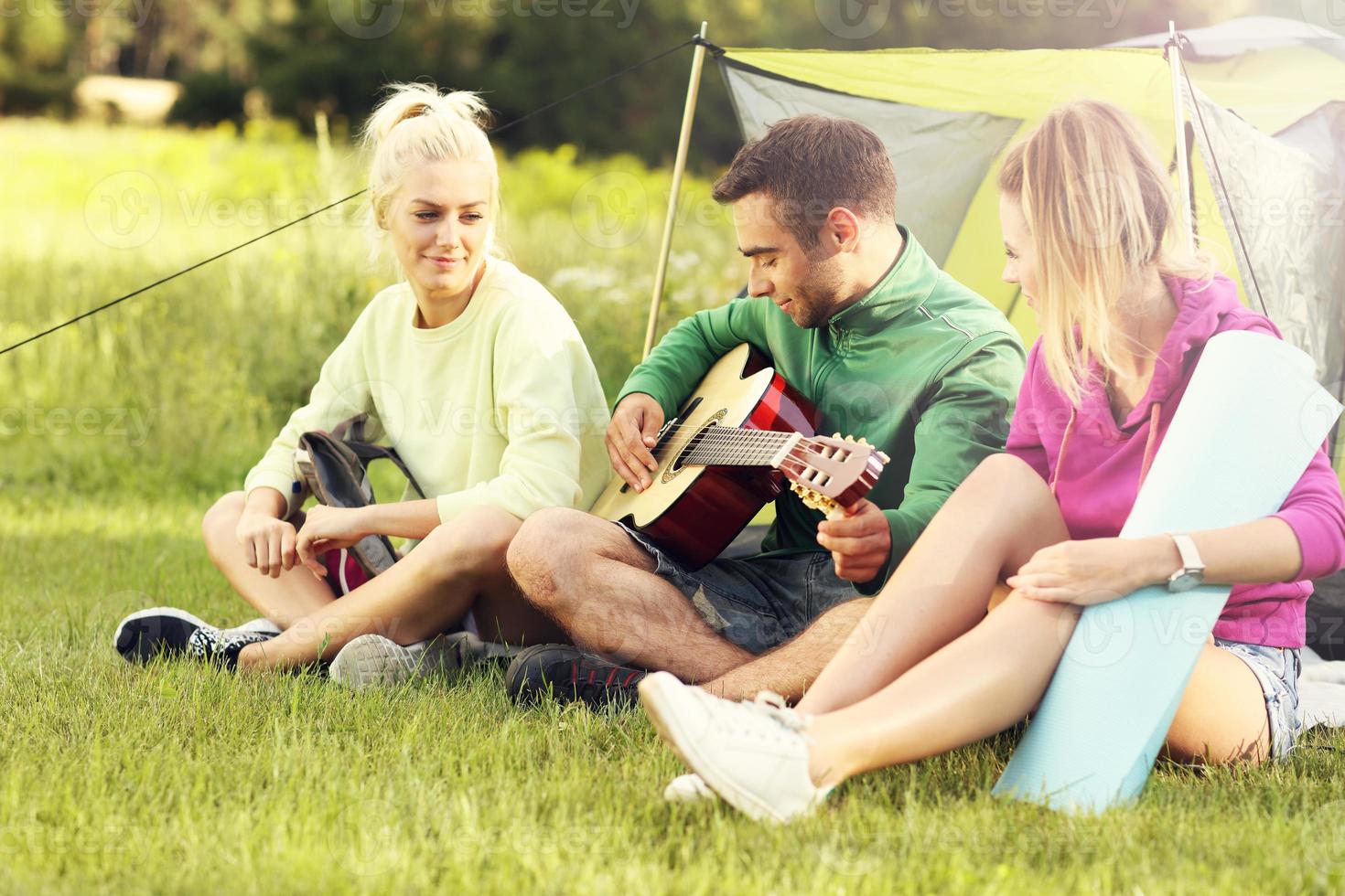 grupp av vänner camping i skog och spelar gitarr foto