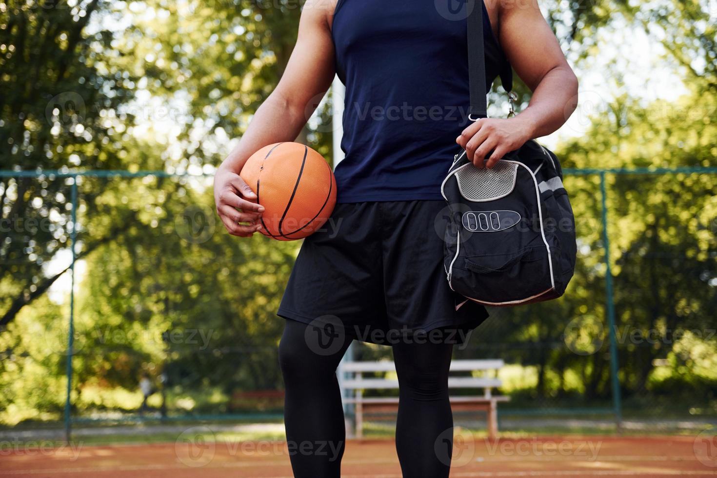 skön grön träd på bakgrund. afrikansk amerikan man spelar basketboll på de domstol utomhus foto