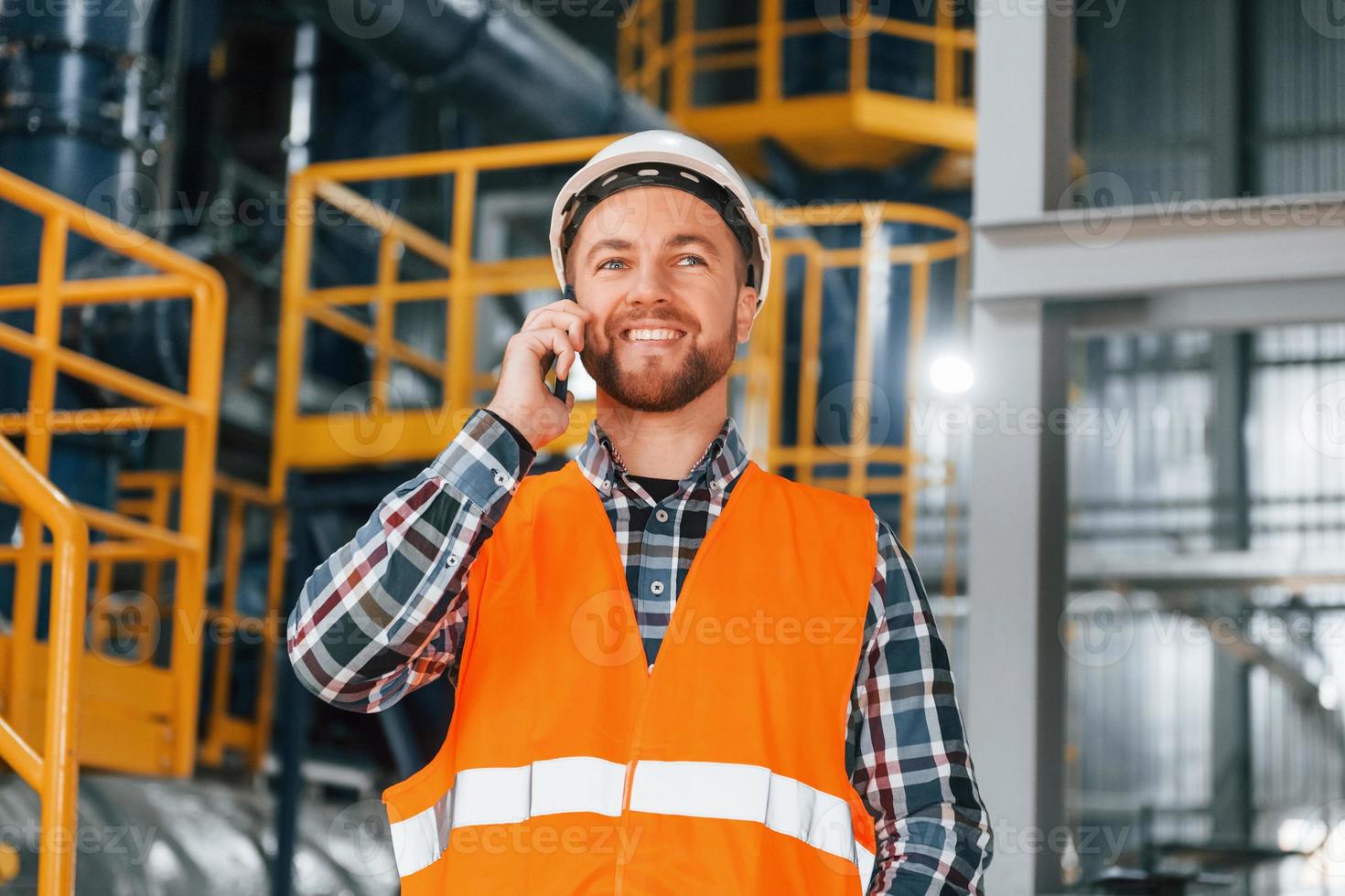 talande förbi telefon. konstruktion arbetstagare i enhetlig är i de fabrik foto