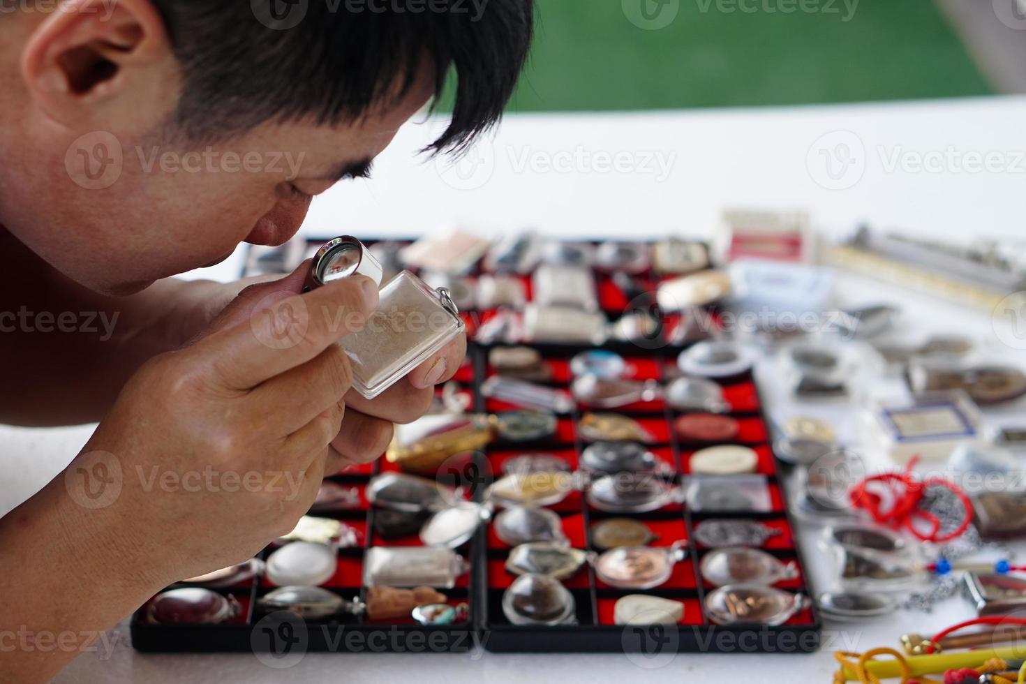 närbild mannens händer håll buddha amulett och förstorande glas till kolla upp detaljer och figur av objekt. begrepp, tro, tro i helig och tur för buddhister. insamling amulett som hobbyer, utbyta, handel. foto